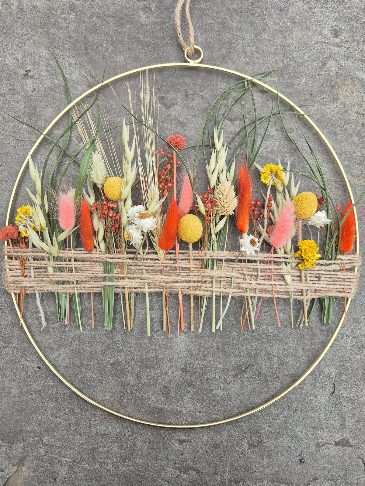 Dried flower hoop with yellow, orange and green flowers resting on a stone background.