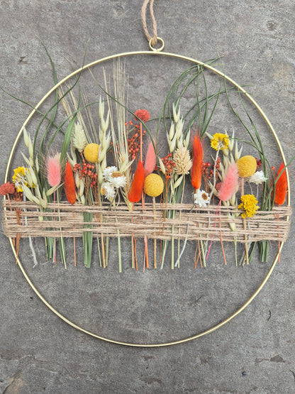 Dried flower hoop with yellow, orange and green flowers resting on a stone background.