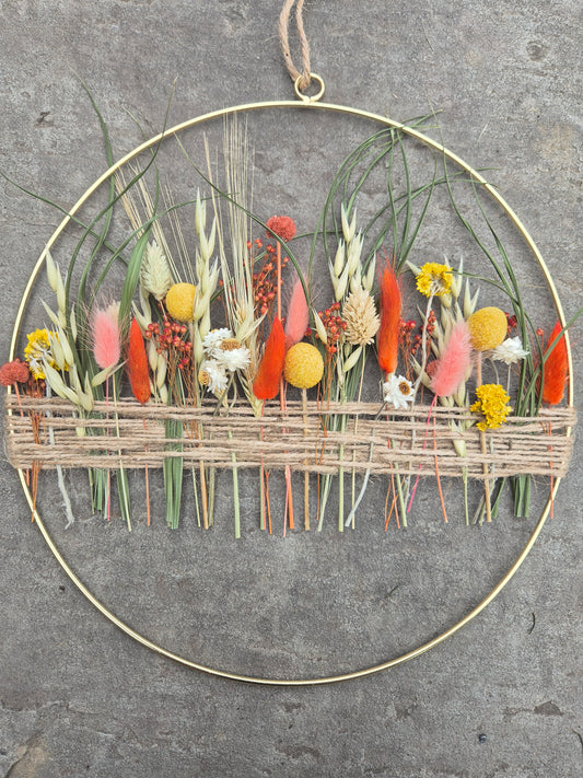 Dried flower hoop with yellow, orange and green flowers resting on a stone background.