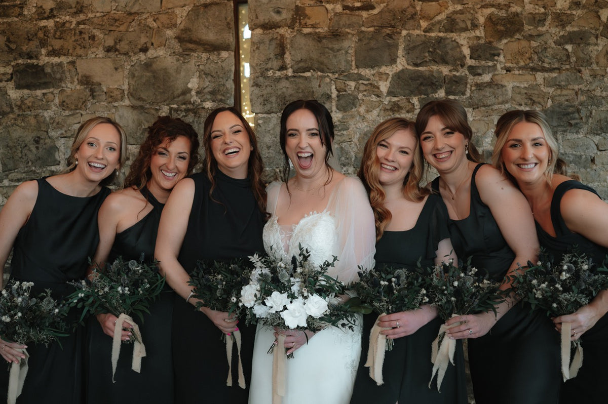 A bride and her bridesmaids smiling in a wedding photo featuring dried and preserved flower bouquets.