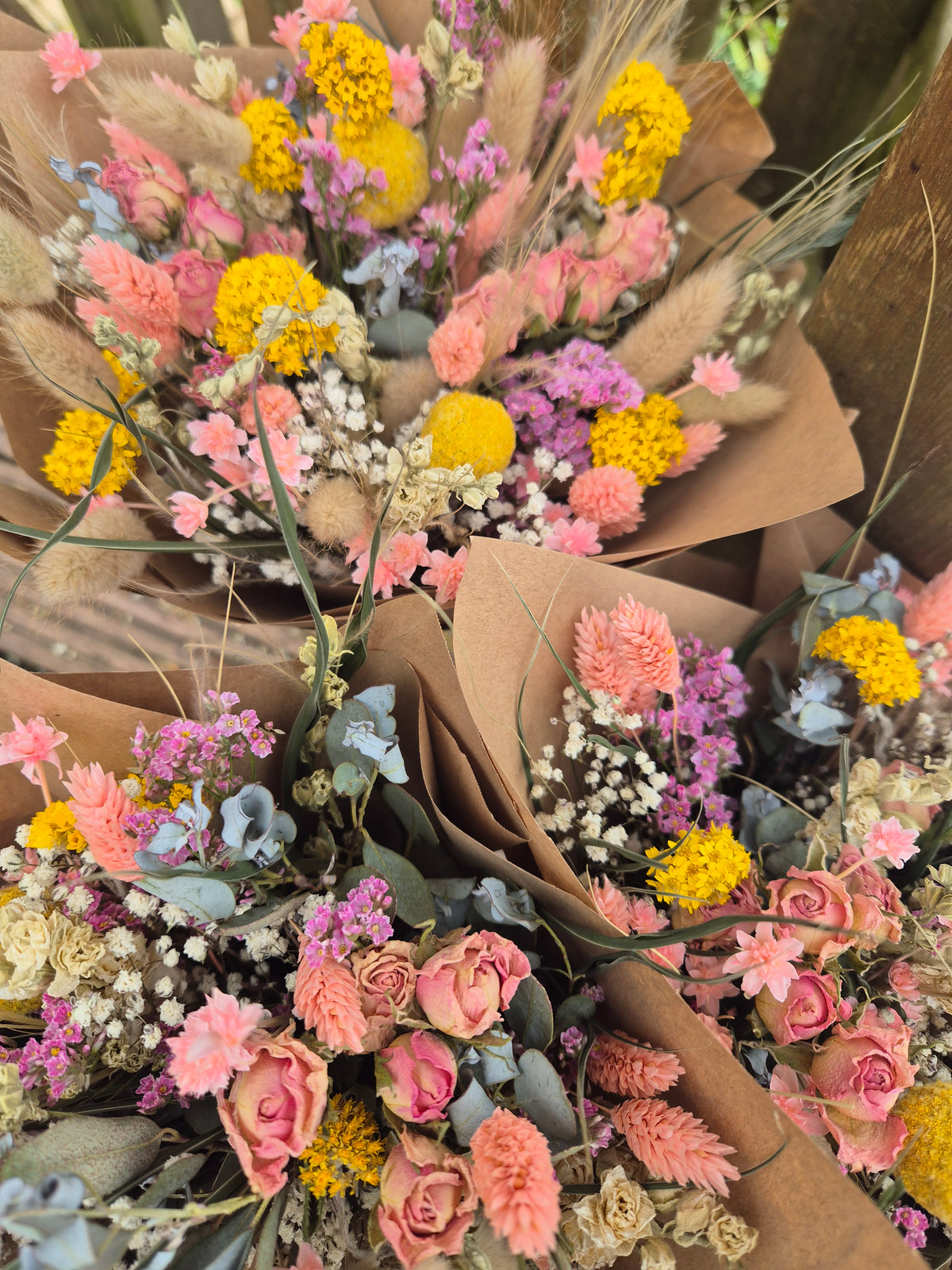 Dried flower bouquet with pink, yellow, and white hues delicately wrapped in brown paper.