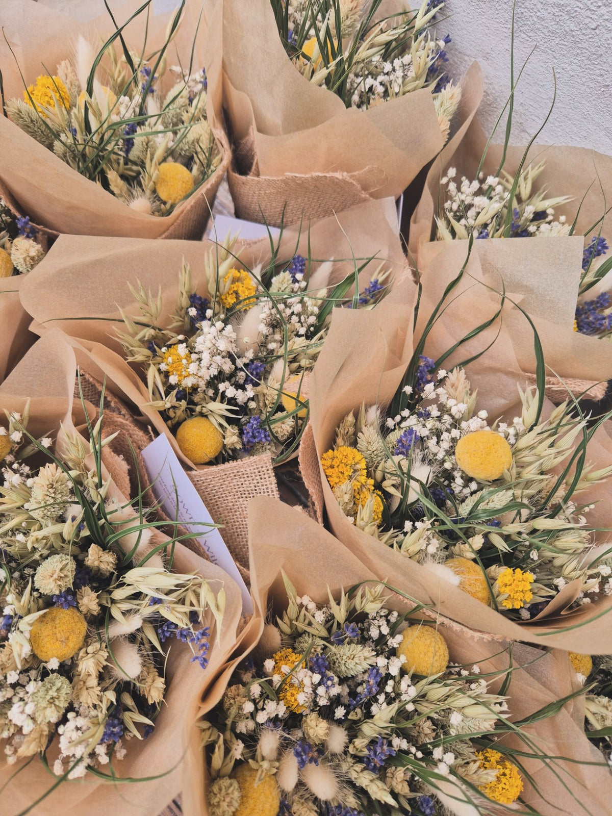 A big selection of bouquets of dried flowers wrapped in brown paper on a textured surface