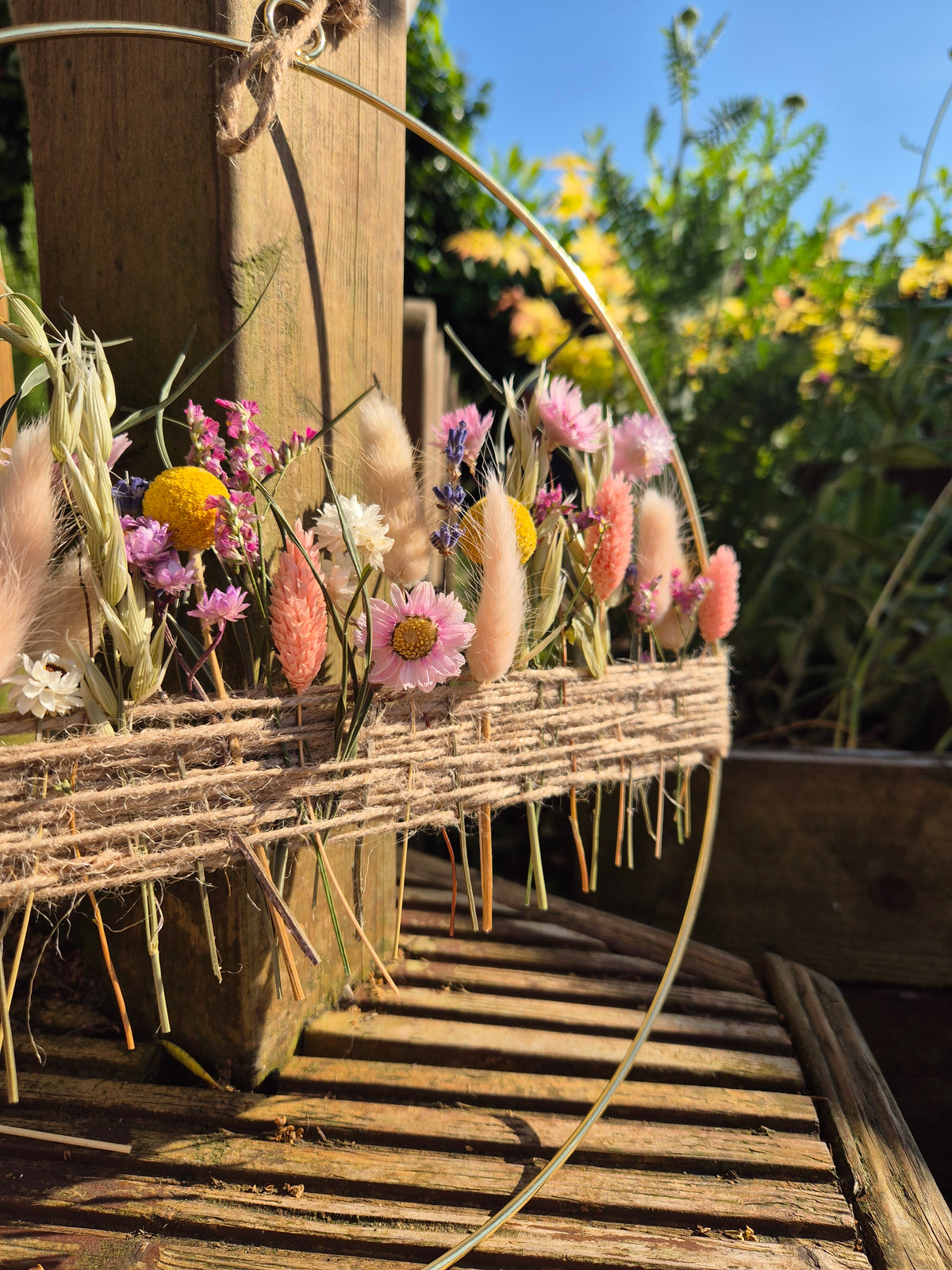 A summer inspired bright and colourful dried flower hoop pictured in a summer garden