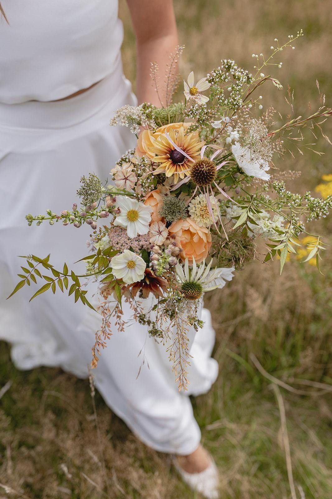 Bouquet of wildflowers held by a person in a white dress outdoors.