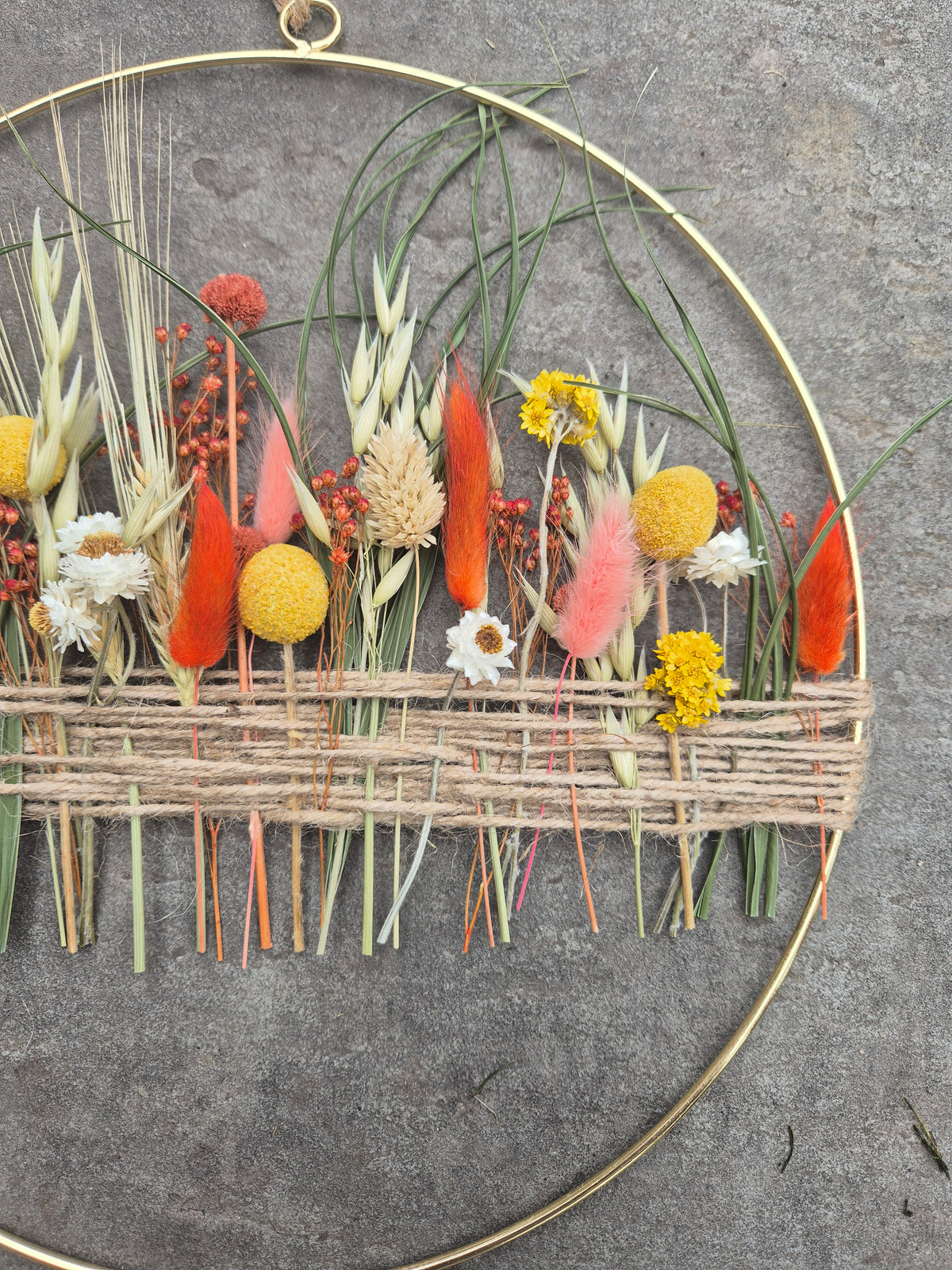 A gold hoop with orange, yellow and green dried flowers.
