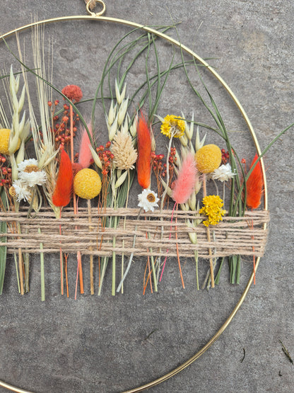 A gold hoop with orange, yellow and green dried flowers.