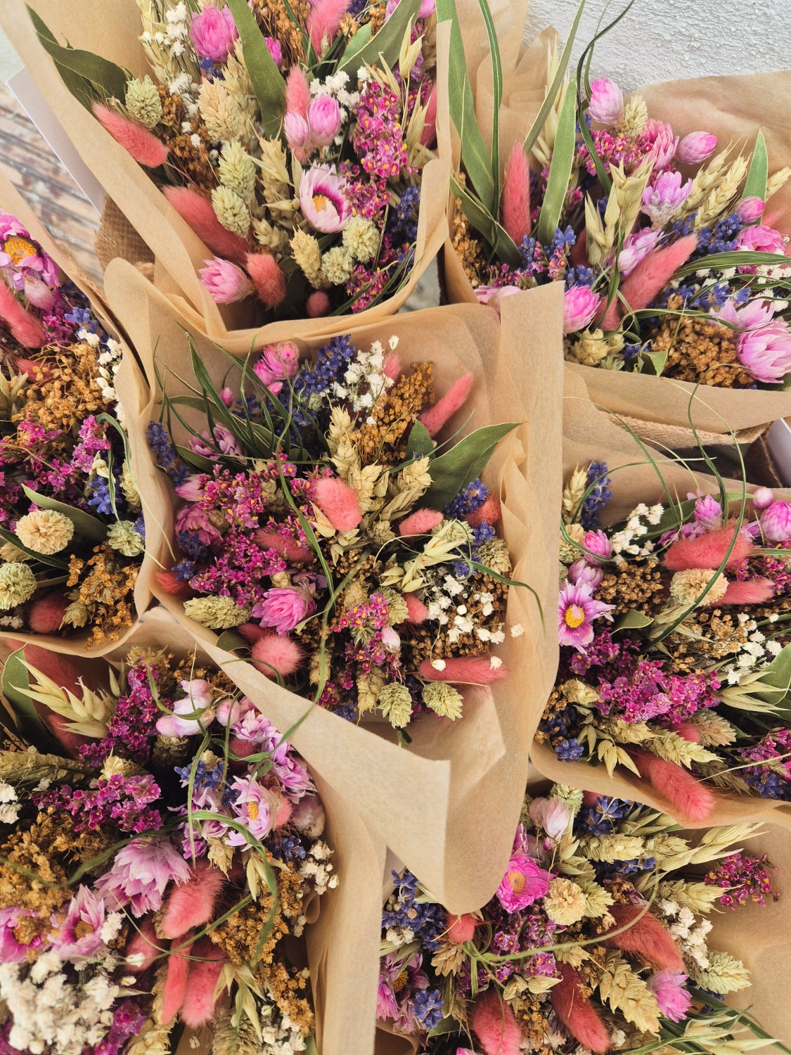 Pink and blue bouquets of colorful dried flowers in brown paper packaging.