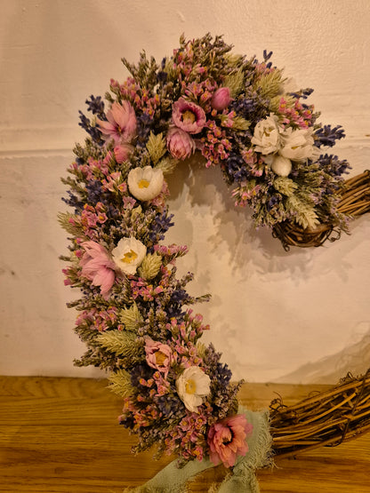 Dried flower wreath with green, blue and pink hues resting on a neutral wall