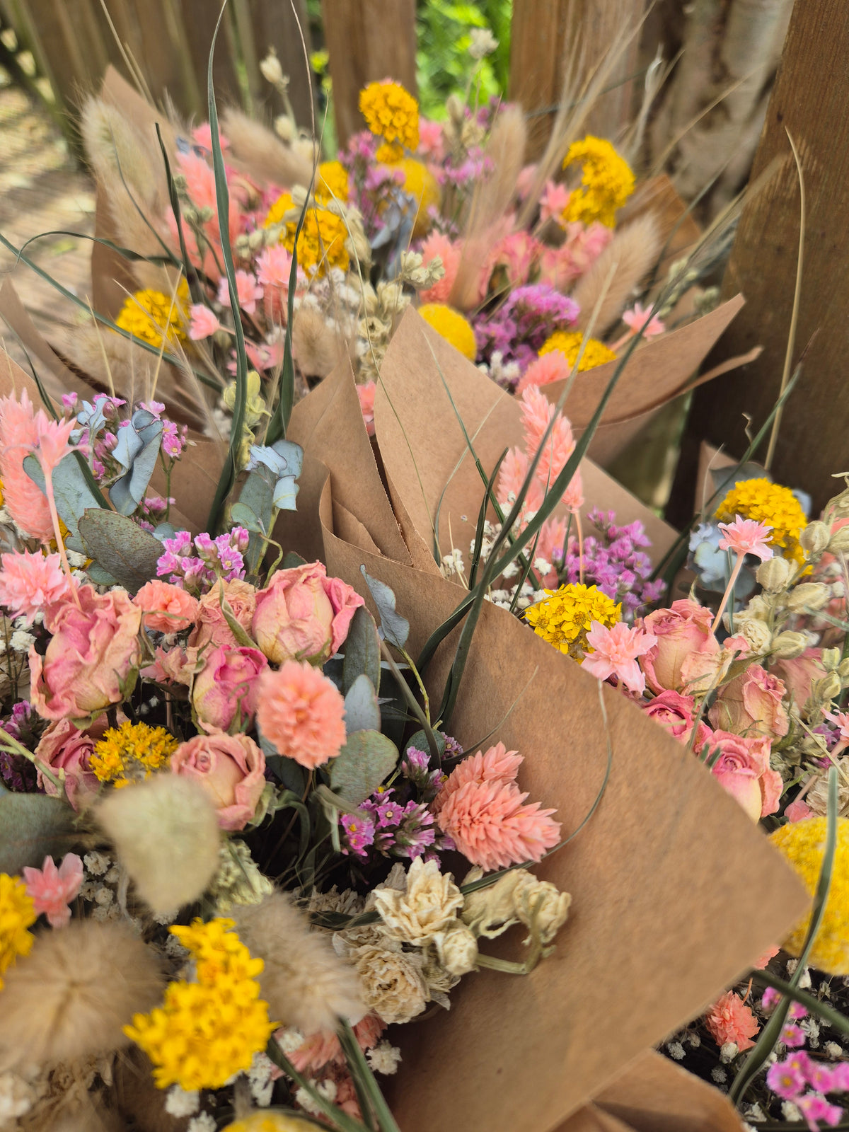 Bouquets of dried flowers with brown paper wrap, featuring pink, yellow, and green colours inspired by the summer.