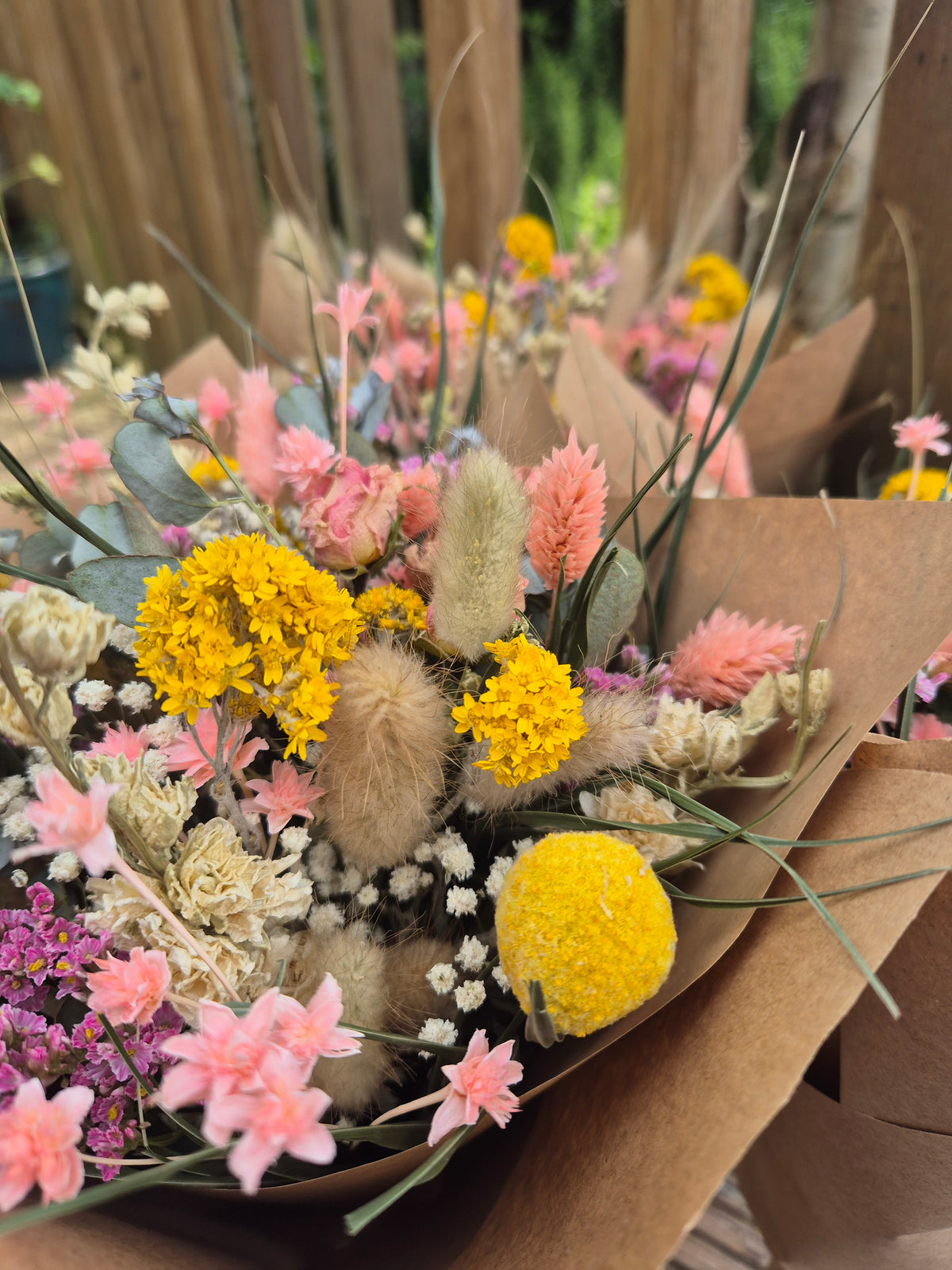 Bouquet of dried flowers with yellow and pink flowers in brown paper packaging.