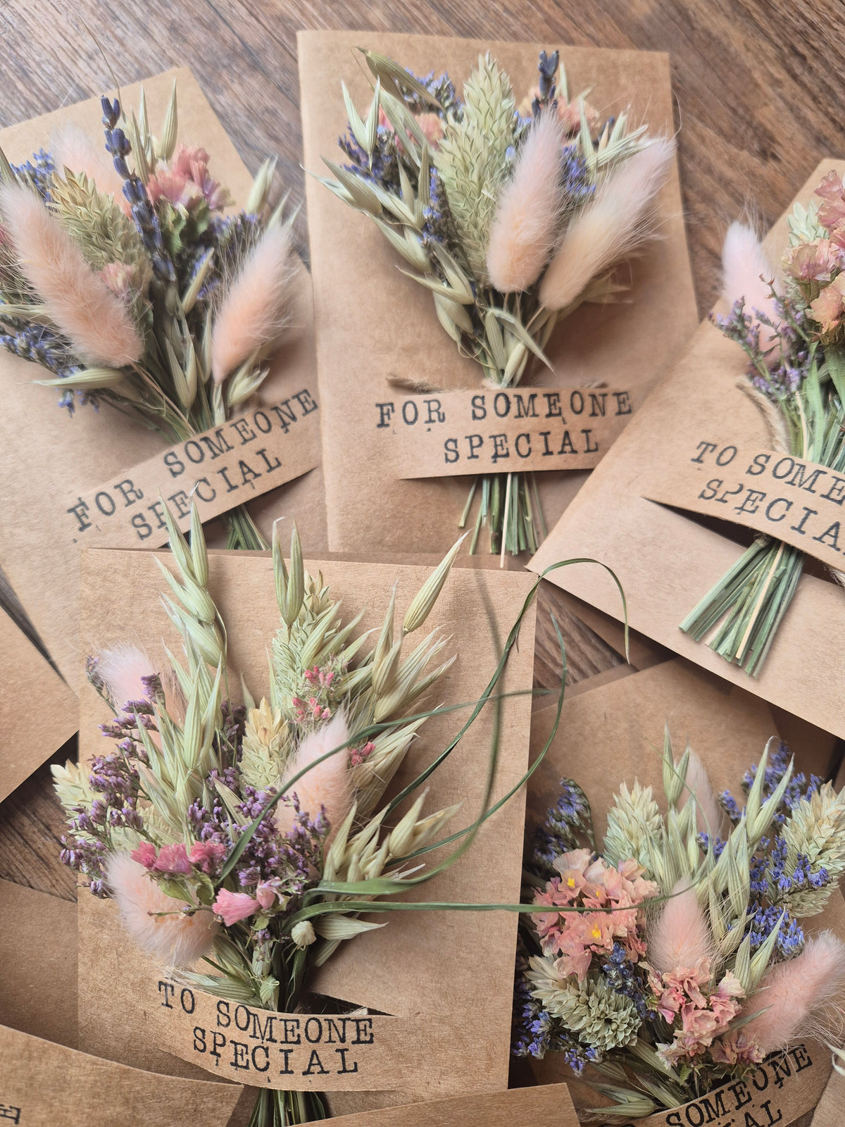 Kraft paper cards with dried floral designs and text on a wooden surface